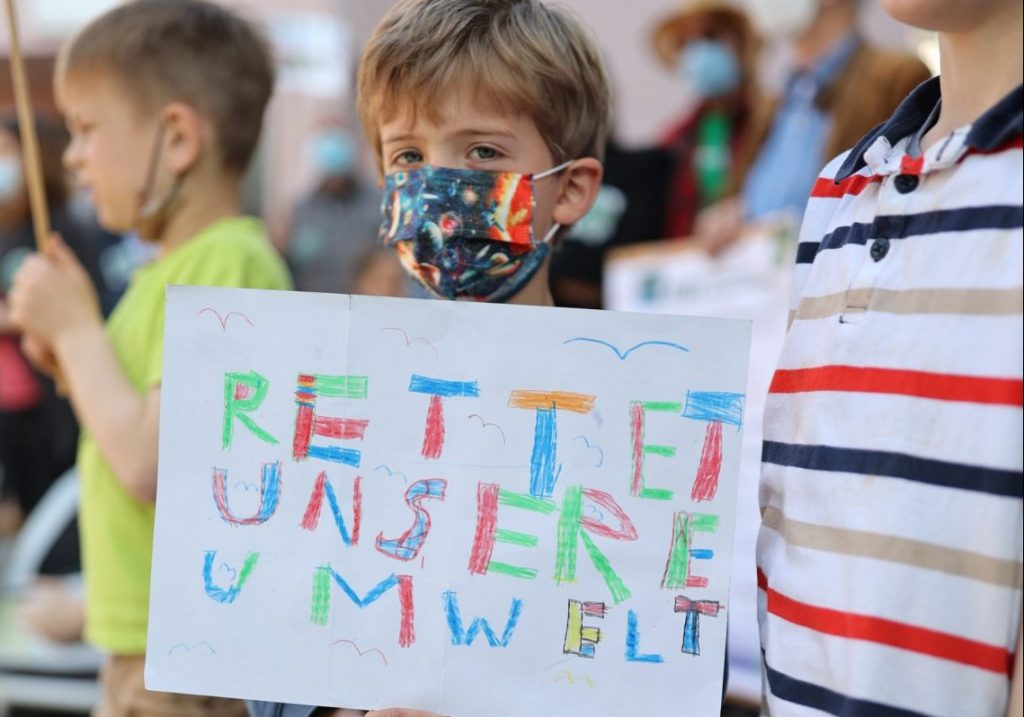 Ein Kind hält ein Demo-Schild mit der Aufschrift "Rettet unsere Umwelt"